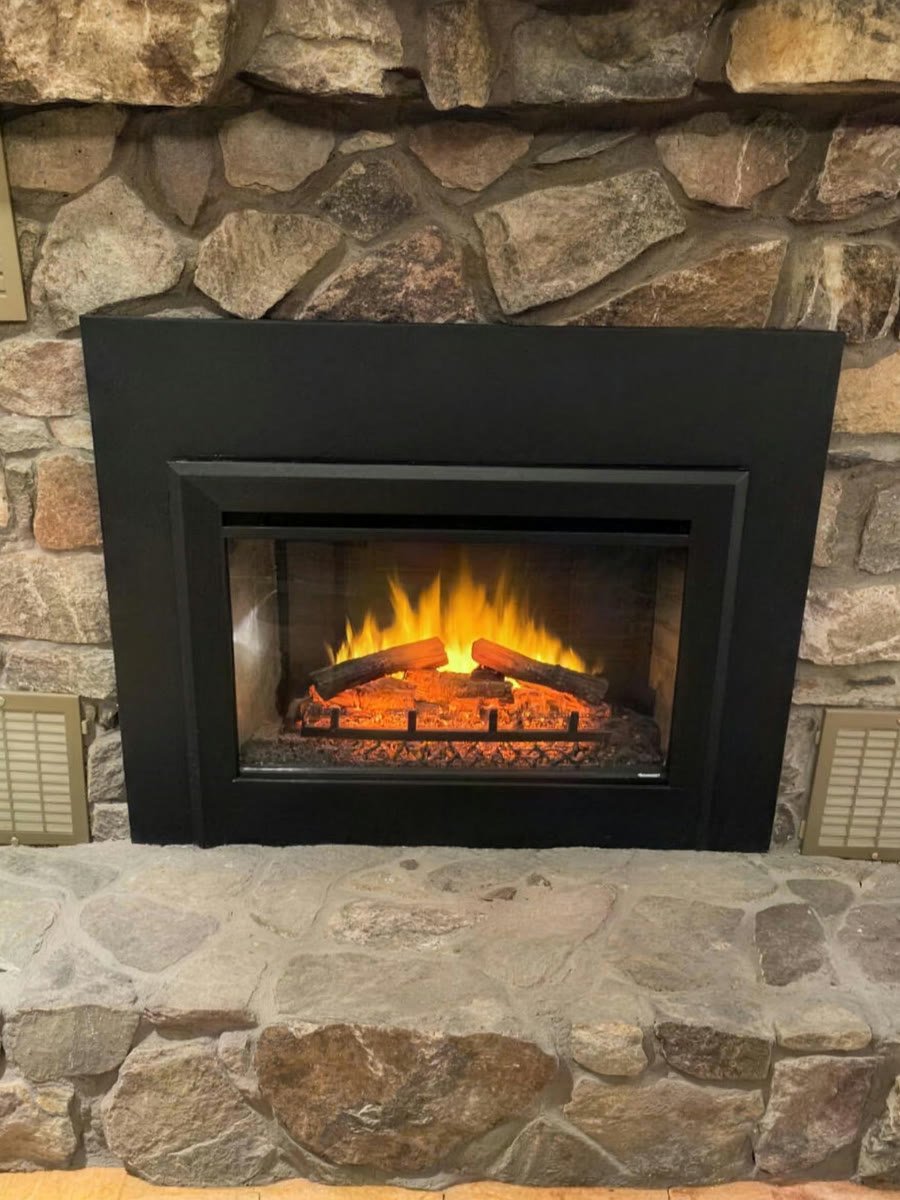 Black gas insert with a lit fire, set in a stacked stone fireplace wall