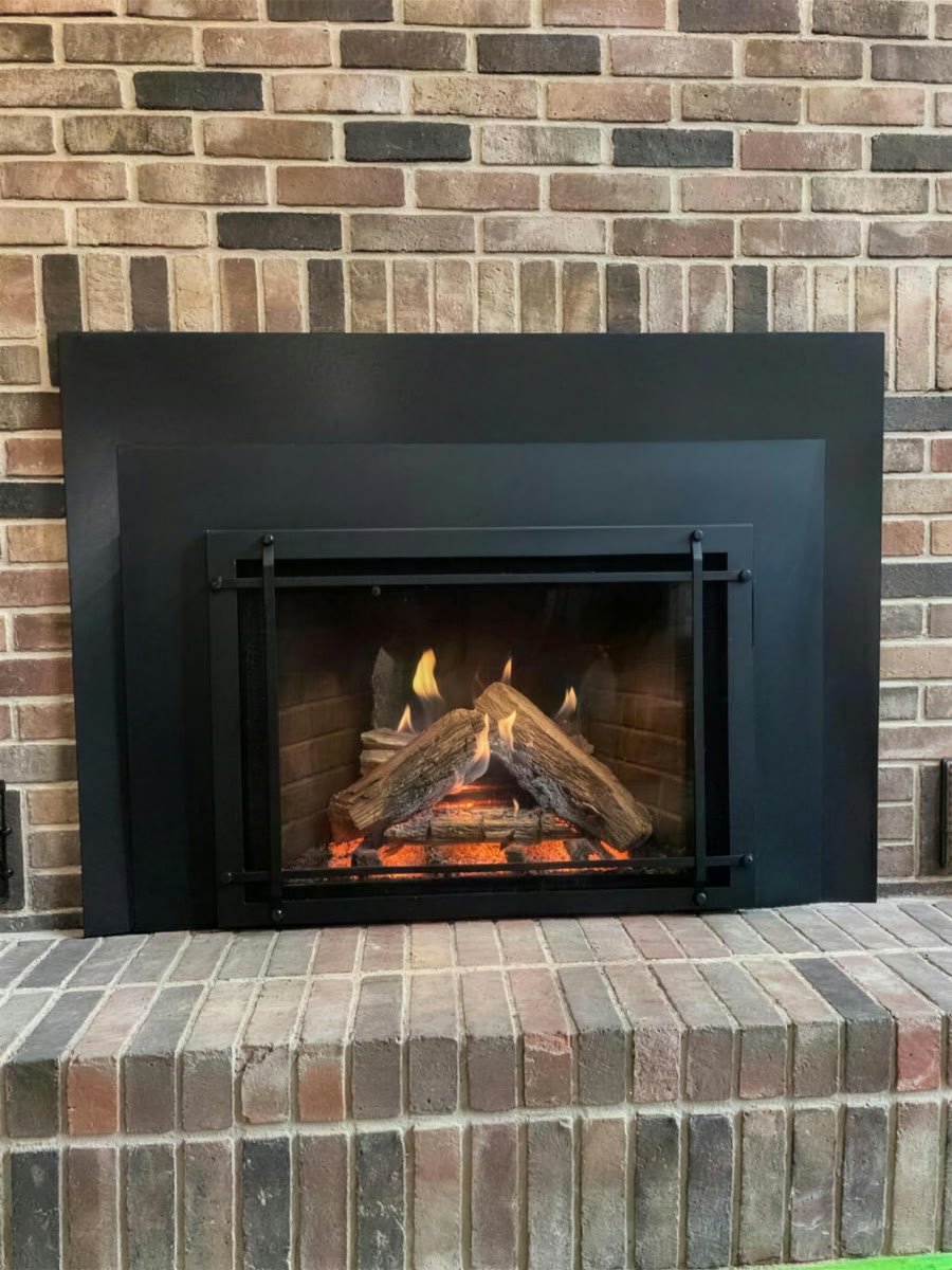Black gas insert with logs and flames in a red brick fireplace