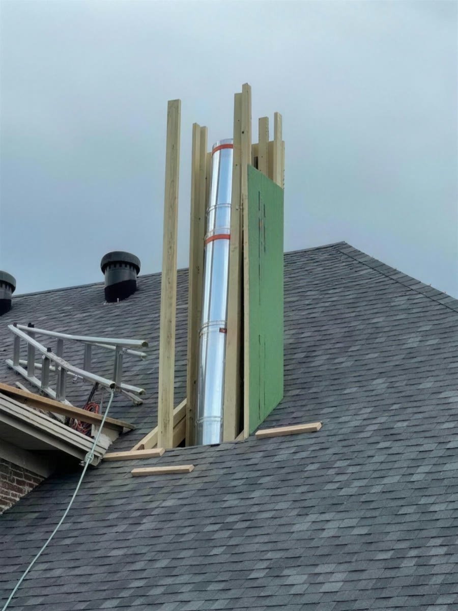 New chimney chase framed in wood around a steel flue pipe on a shingle roof